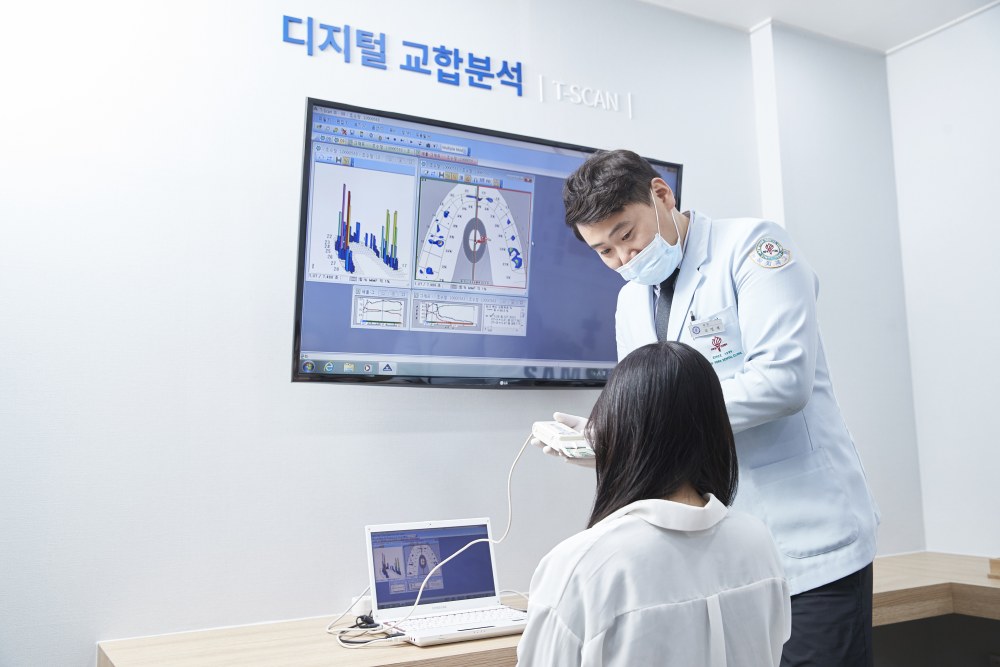 환자가 디지털 교합분석 장비 티스캔(T-Scan) 센서를 물고 검사받는 모습, 화면에 교합력 분포가 표시되어 있다