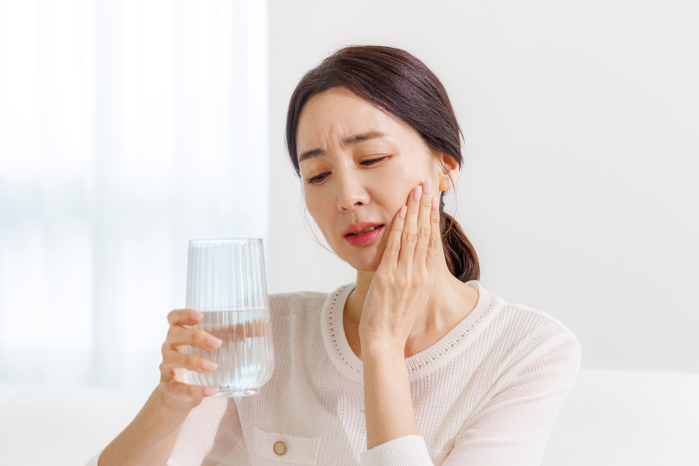 찬물을 마시고 치아가 시려 턱을 감싸고 있는 중년 여성
